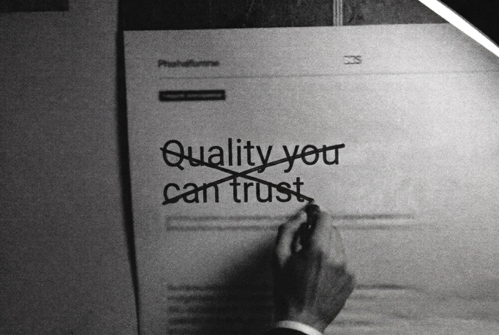 A hand striking through the printed headline 'Quality you can trust.' with a marker under a work lamp