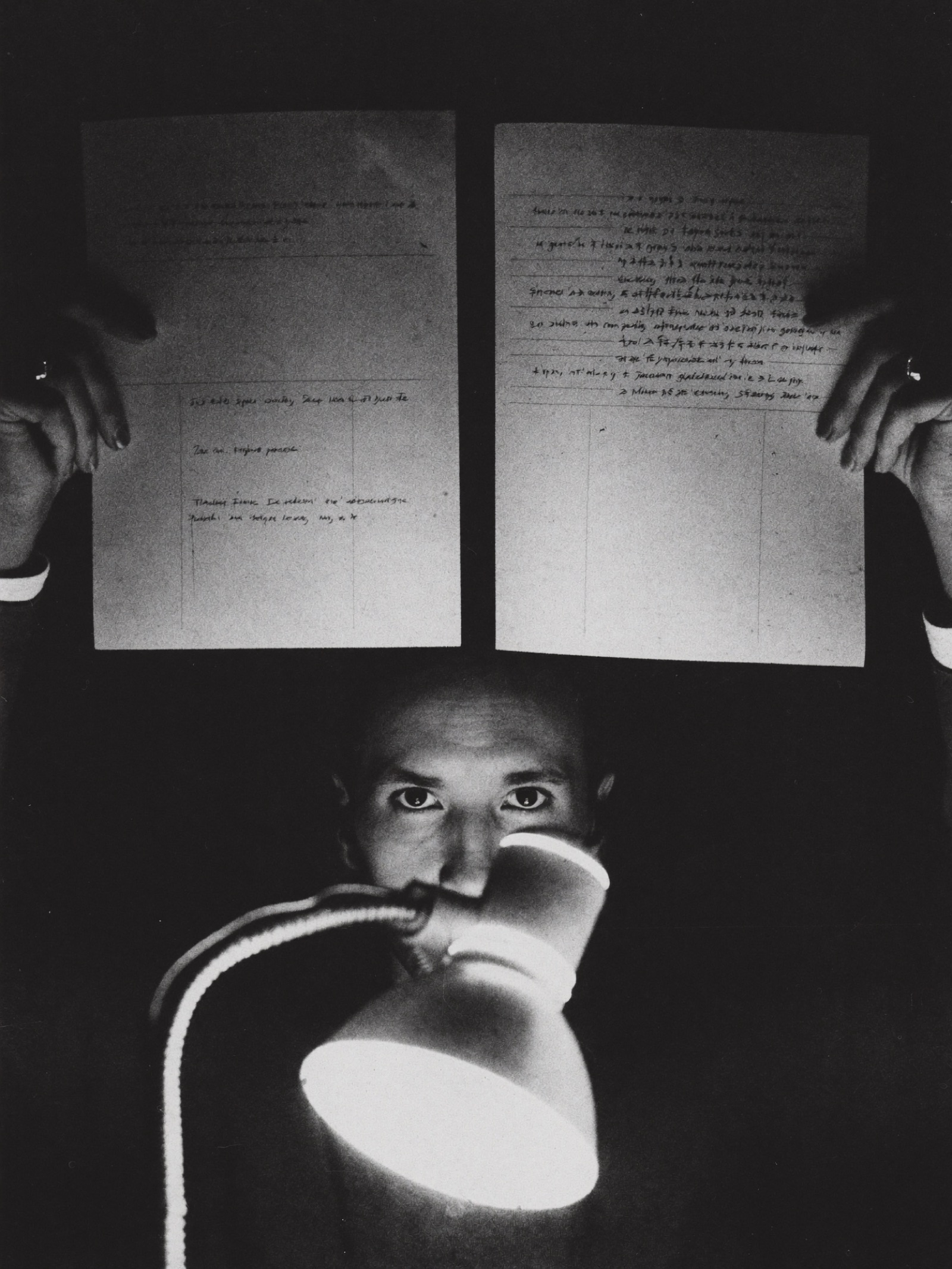 A person comparing two printed pages side by side against the light of a work lamp